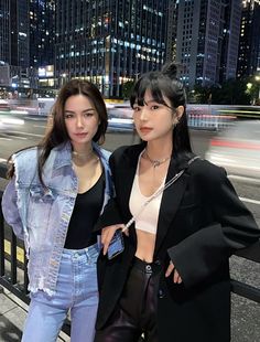 two young women standing next to each other in front of a city street at night