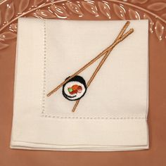 two chopsticks on top of a white napkin with a sushi embroidered on it