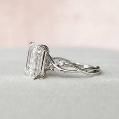 an engagement ring with a large emerald cut diamond on it's shants, sitting on a white surface