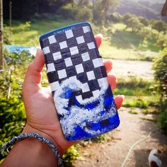 a hand holding up a cell phone covered in blue and white paint with a checkered design on it