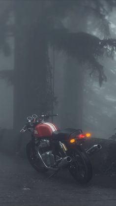 a red motorcycle parked in the middle of a forest on a dark foggy day