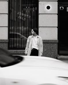 a man standing next to a white car in front of a tall building on a city street