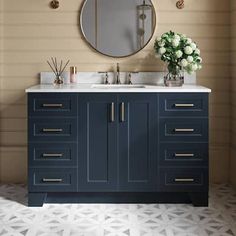 a bathroom vanity with two sinks and a round mirror above it, in front of a beige wall