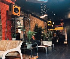 a living room filled with lots of furniture and speakers on top of brick wall next to potted plants