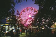 a ferris wheel is lit up at night in an amusement park with people milling about