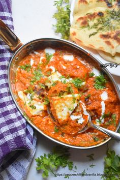 a pan filled with meat and sauce next to some flat bread on a white table