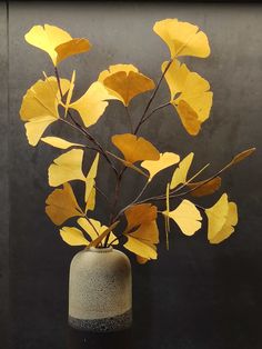 a vase filled with yellow leaves on top of a black table next to a wall