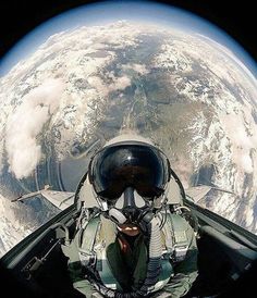 the view from inside an airplane looking down at earth and sky, with a pilot wearing goggles