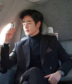 a man in a suit sitting on an airplane holding a cell phone to his ear