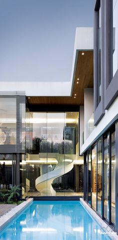 an empty swimming pool in front of a modern house with glass walls and stairs leading up to the upper floor