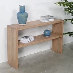 a wooden table with two books and a vase on the shelf next to it in front of a white wall