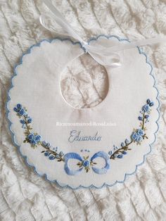 a baby bib with blue flowers on it and a ribbon hanging from the back