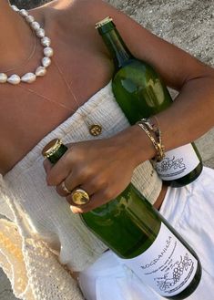 a woman sitting on the ground holding two bottles of wine in one hand and a ring on her finger