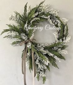 a christmas wreath hanging on the wall with white and green foliage, ribbon and bow