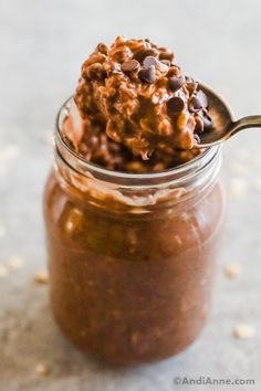 a spoon full of chocolate pudding in a glass jar with some oats on top