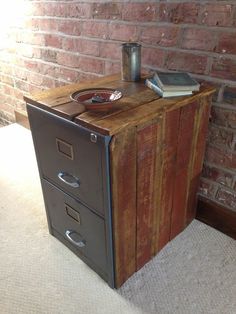 an old wooden filing cabinet with two drawers and a book on top, in front of a brick wall