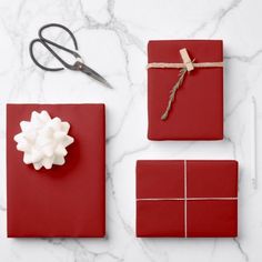 red wrapping paper, scissors and other items on a white marble counter top with a gift wrapped in gold ribbon