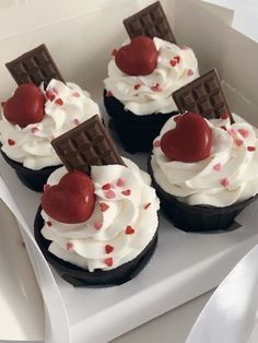 four cupcakes with white frosting and red hearts on top in a box