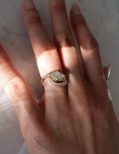 a woman's hand with a diamond ring on her left hand, and a white marble surface in the background