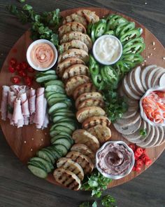 an assortment of meats and vegetables on a wooden platter with dip sauces