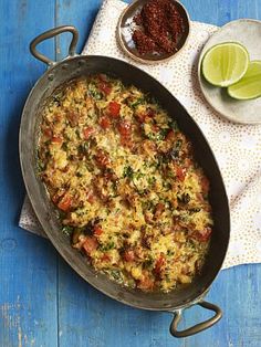 a skillet filled with rice and vegetables next to a bowl of lime wedges