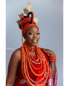 a woman wearing an orange and gold headdress with beads around her neck, smiling at the camera