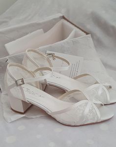 a pair of white wedding shoes sitting on top of a bed next to a box