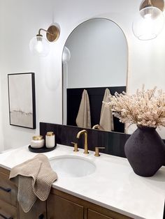 a bathroom with a sink, mirror and vase on the counter top in front of it