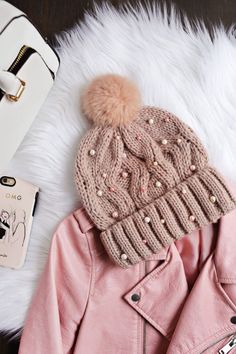 a pink jacket, hat and cell phone on top of a white furnishing