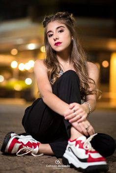 a young woman sitting on the ground with her legs crossed and wearing red and white sneakers