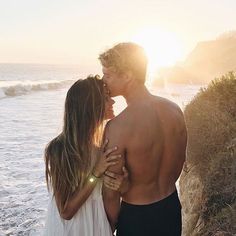 two people standing next to each other in front of the ocean with sun shining on them