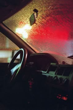 the interior of a car with rain drops on the windshield and red lights behind it