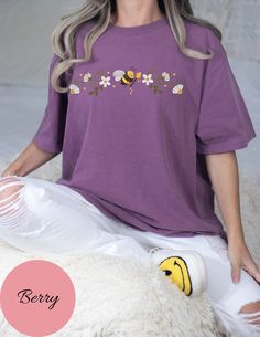 a woman sitting on top of a bed next to a white teddy bear and wearing a purple shirt