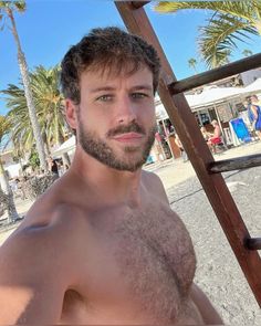 a man with no shirt on standing in front of palm trees and looking at the camera