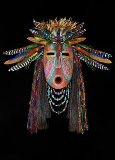 a colorful mask with feathers on it's head is shown against a black background