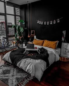 a bedroom with black walls and wooden floors has a large bed, two windows, an office desk, and a bike hanging from the ceiling