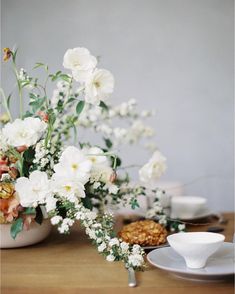 white flowers are in vases on a table with other plates and cups around them