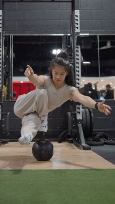 a woman is doing a trick on a ball in the middle of a crossfit gym