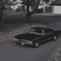 an old black car is parked on the side of the road in front of a house