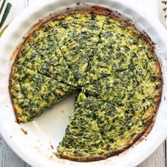 a spinach quiche in a white dish with one slice missing