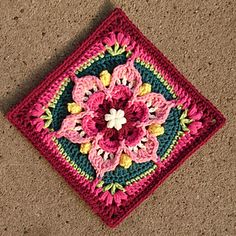 a crocheted square with a flower on the center in pink, green and yellow