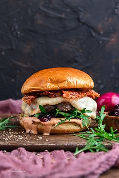 a bacon cheeseburger is sitting on a cutting board with fresh herbs and sauce