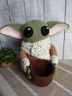 a crocheted baby yoda doll sitting next to a potted plant