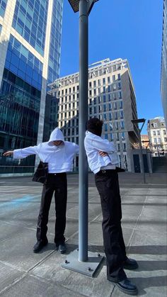 two men standing next to each other under a street light with buildings in the background