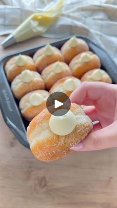 a person holding a donut in front of a pan filled with doughnuts