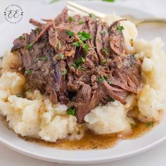 a white plate topped with meat and mashed potatoes covered in gravy next to a fork