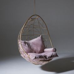 an egg chair hanging from a string with pillows on the bottom and back, in front of a gray background