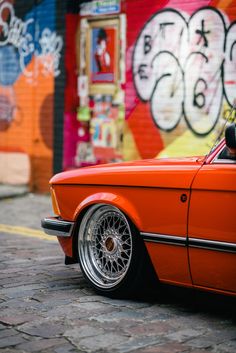 an orange car parked in front of a graffiti covered wall