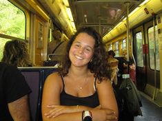 a woman sitting on a bus with her arms crossed and looking at the camera smiling