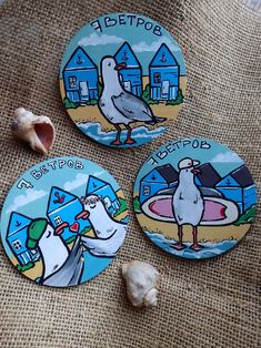 three coasters with birds on them sitting on a table next to shells and seashells